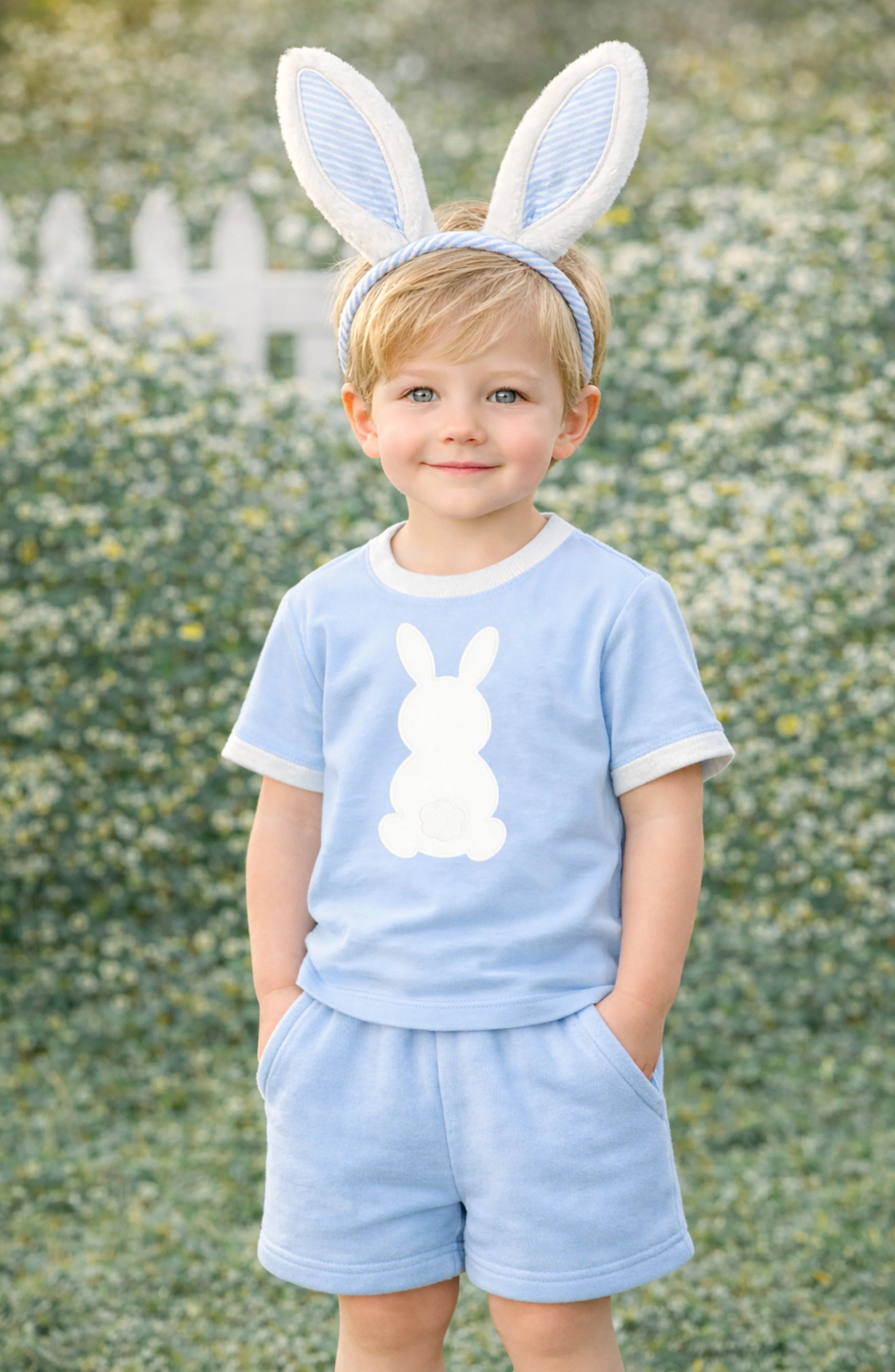 Child wearing a light blue outfit with a bunny design and bunny ears outdoors.