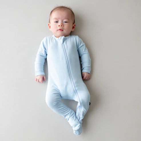 Baby wearing a light blue onesie on a plain background