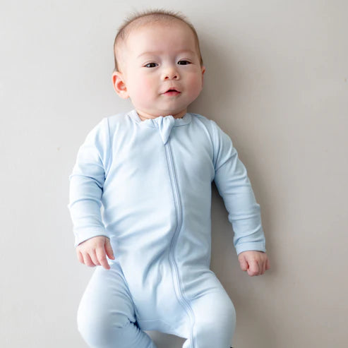 Baby wearing a light blue onesie against a plain background