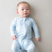 Baby wearing a light blue onesie against a plain background