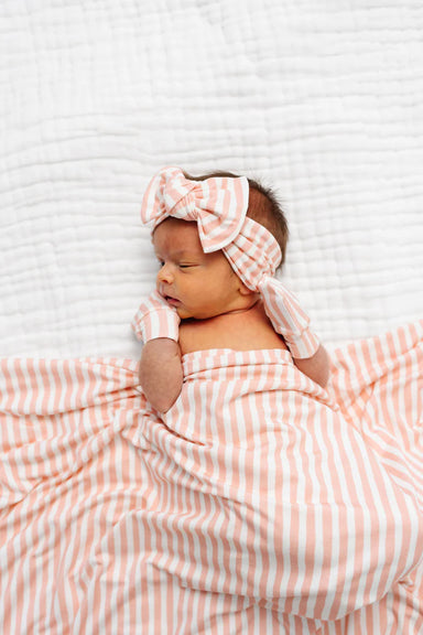 Newborn baby wrapped in a orange and white striped blanket with a matching headband on a white background.
