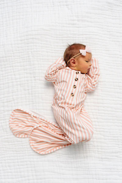 Newborn baby wrapped in a orange and white striped swaddle on a white textured surface