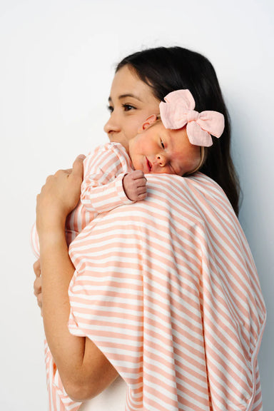 Woman holding a baby wrapped in a orange and white striped blanket against a light gray background