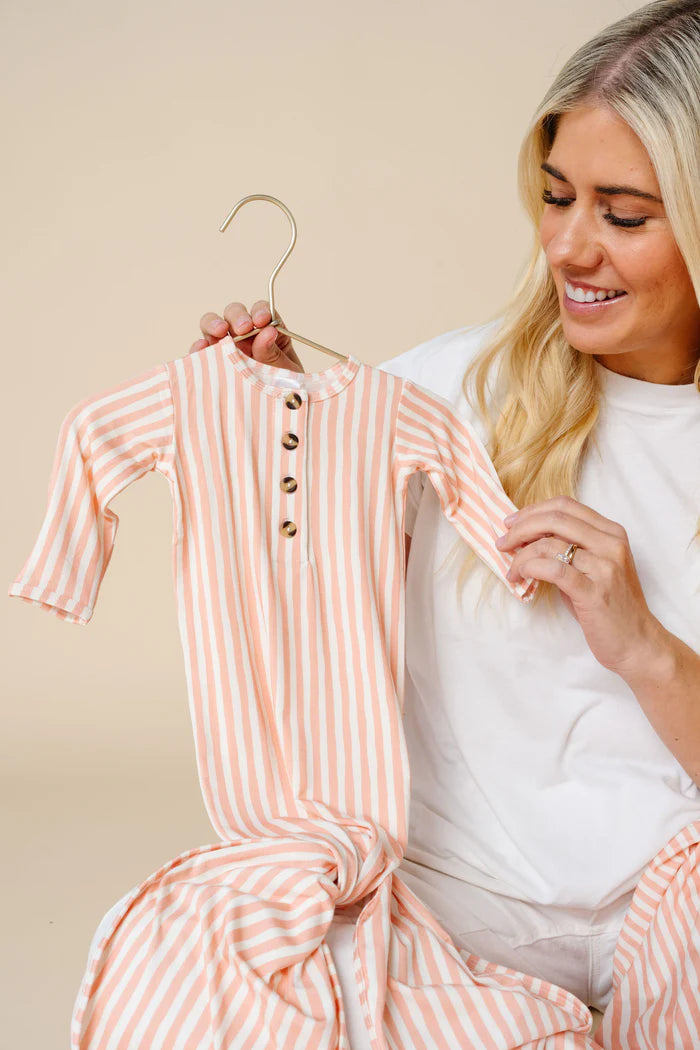 Woman holding a orange and white striped baby outfit on a hanger against a beige background