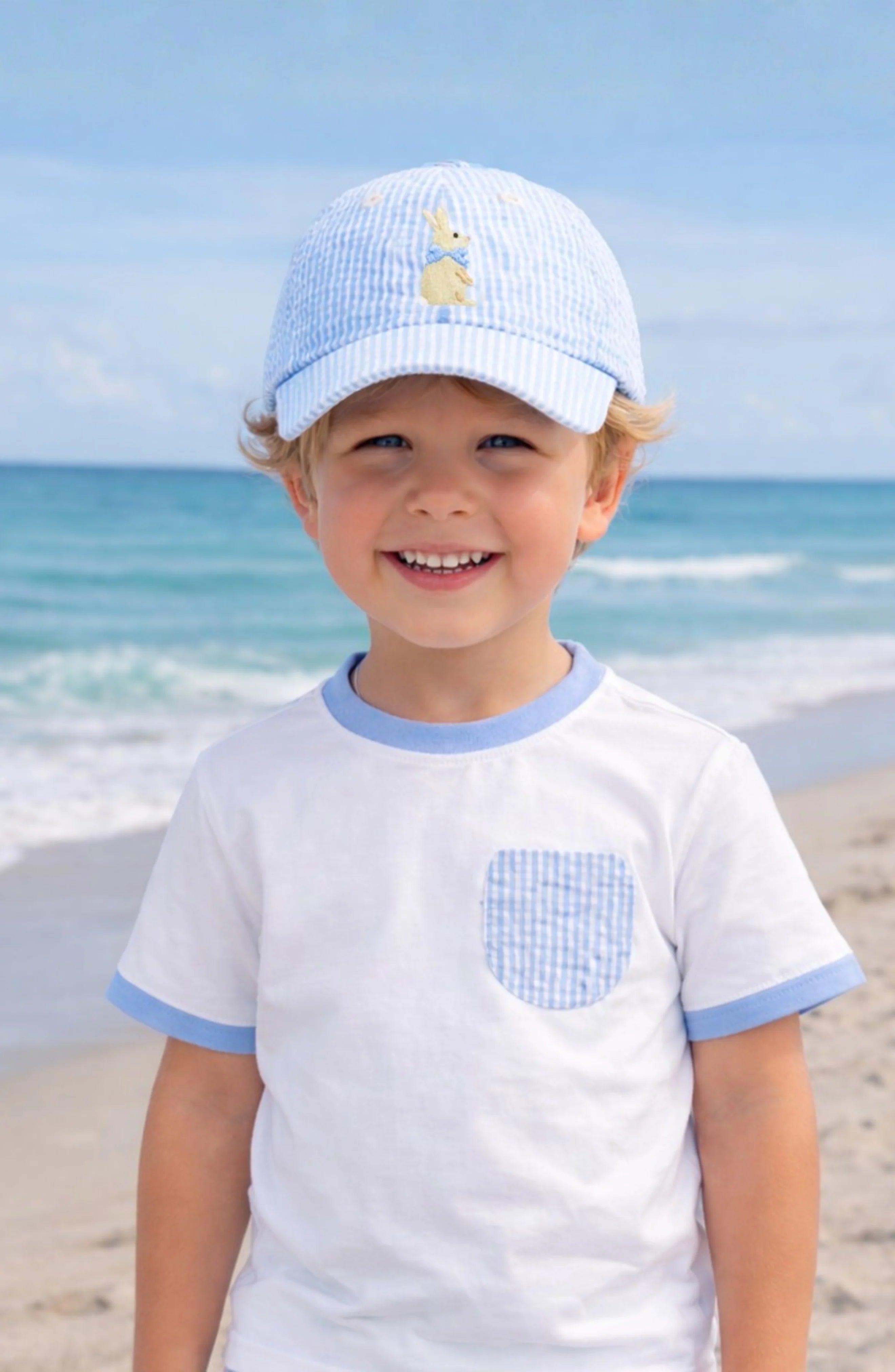 Young boy wearing a light blue cap and matching shirt on a beach