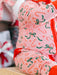 A close-up of a baby wearing a pink one-piece pajama with a festive holiday print of candy canes, green bows, and white snowflakes, paired with a bright red blanket.