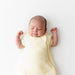 Newborn baby swaddled in a yellow sleep bag on a white background