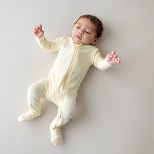 Baby in a cream-colored onesie lying on a light gray surface