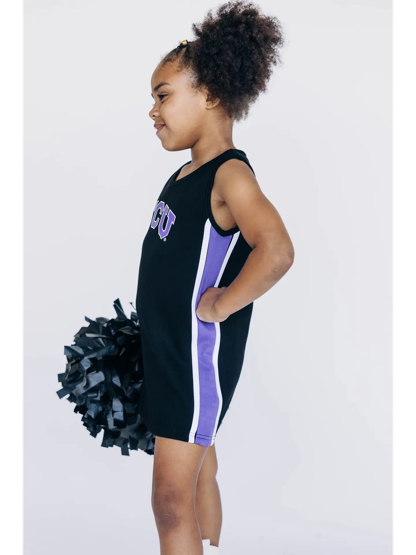 Young girl in a black and purple cheerleading outfit with pom-pom on a white background