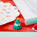 Small Christmas tree decoration with a yellow star on a red checkered tablecloth, with a tube of glue and a colorful plate in the background.