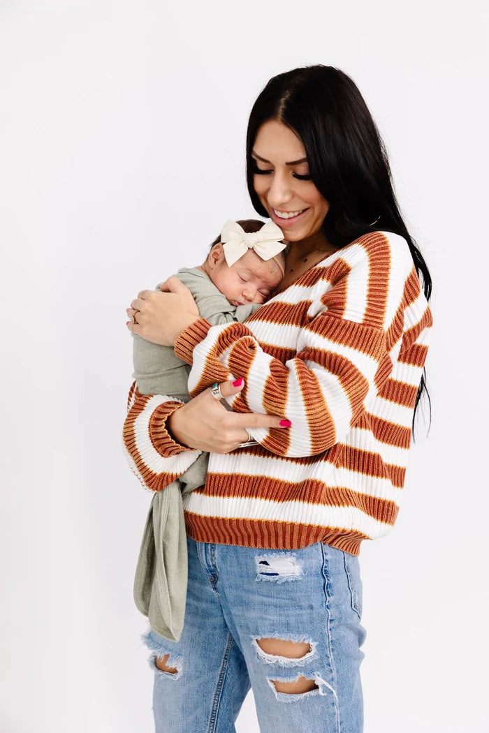 Woman wearing a striped sweater holding a baby against a white background