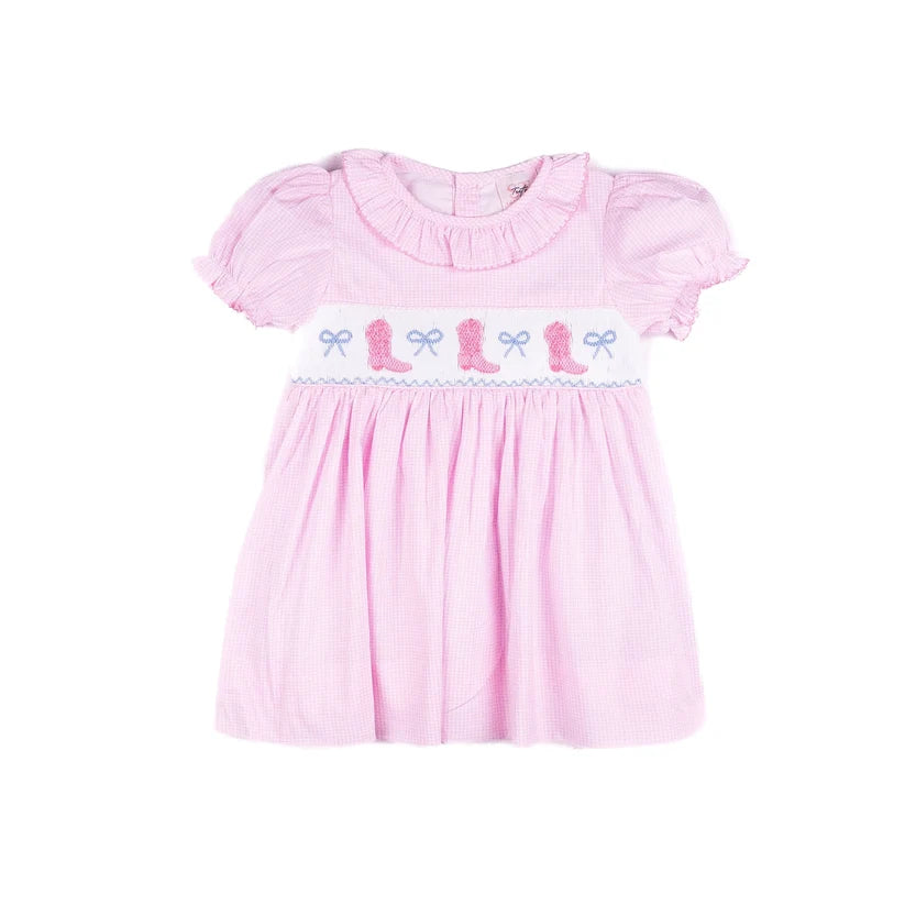 A pink gingham baby dress with short puff sleeves, a ruffled collar, and smocked details across the chest featuring pink cowboy boots and blue bows on a white band.