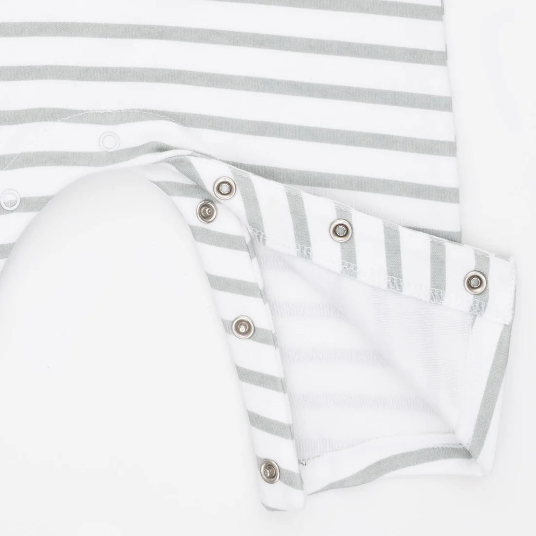 Close-up of a baby garment with white and light gray horizontal stripes, featuring a folded cuff with metal snap buttons on a white background.