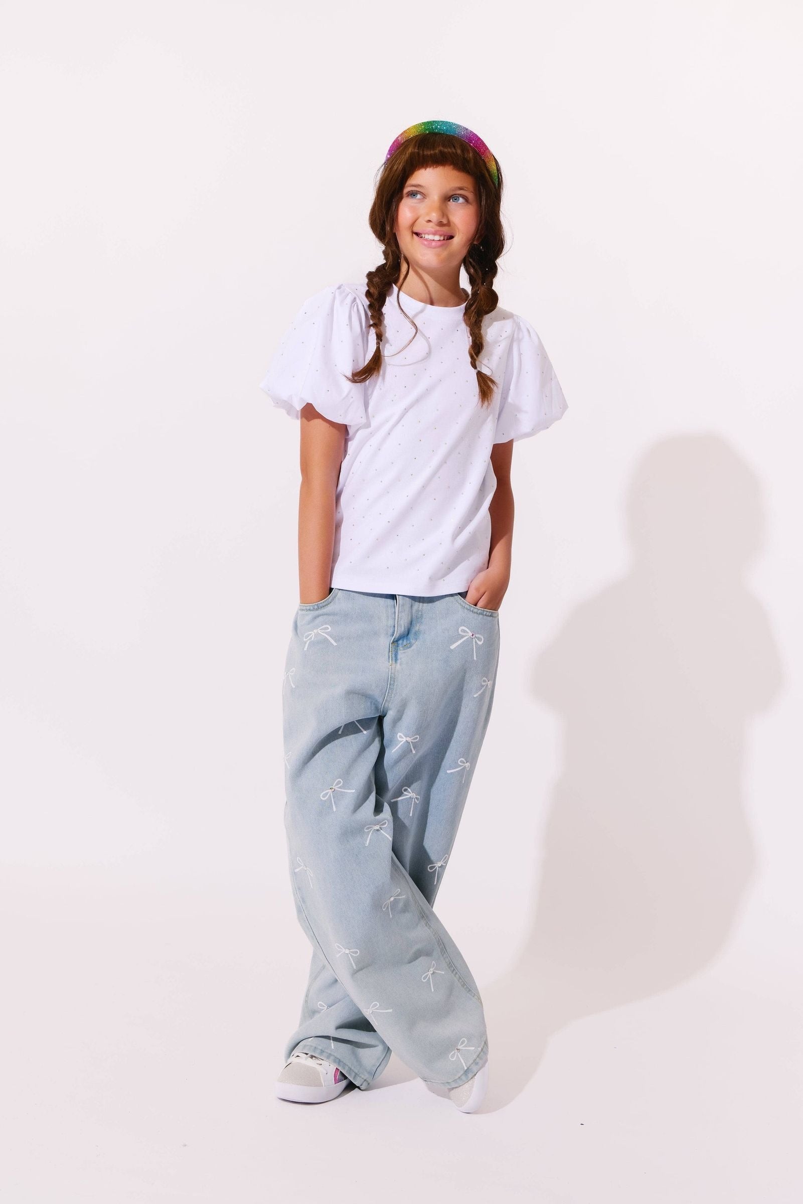 Child wearing a white t-shirt and light blue jeans with a colorful hat on a white background