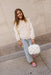 Young girl in a white fleece jacket and light blue jeans holding a polka dot bag against a beige wall.