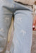 Close-up of light blue denim jeans with small white embroidered bow details scattered across the legs, worn by a model whose hand is visible at the side.