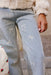 Close-up of a person wearing light blue jeans with small white embroidered bow motifs, paired with a cream fuzzy top and a strawberry-patterned bag.