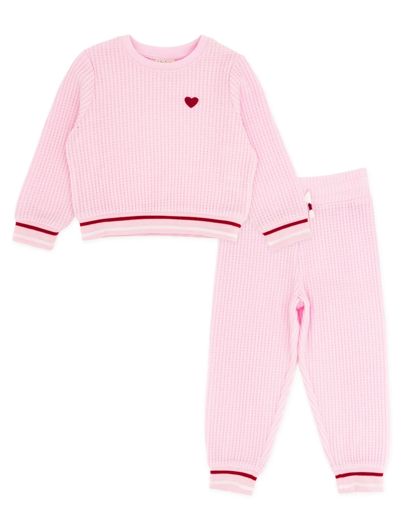 A two-piece baby loungewear set in light pink waffle knit, featuring a long-sleeve top with a small red heart on the chest and matching jogger pants with red striped cuffs.