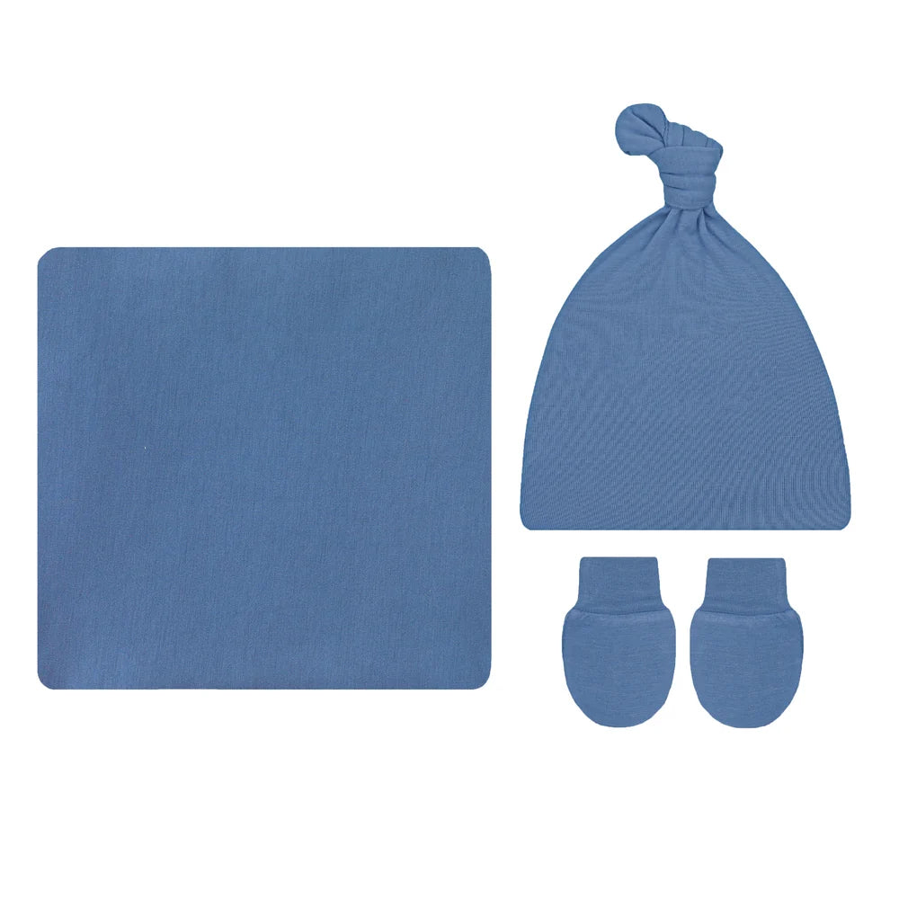 A baby gift set featuring a square blue blanket, a knotted blue beanie hat, and a pair of matching blue mittens, all laid out on a plain white background.