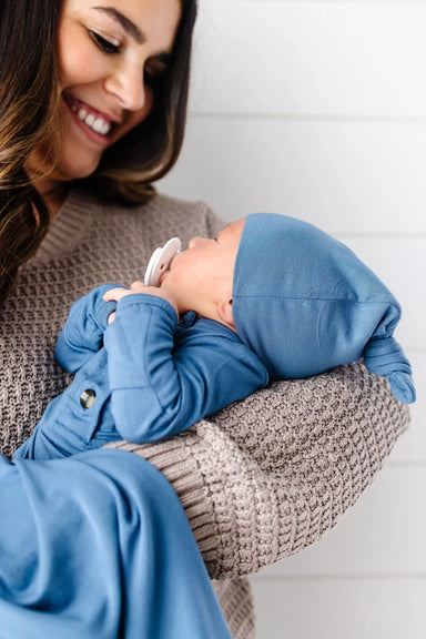 A dusty blue knit baby hat with a knotted top, shown against a plain white background.