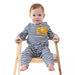 A baby sitting on a wooden chair wearing a navy and white striped long-sleeve romper with a yellow construction graphic on the chest, photographed against a solid white background.