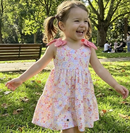 Child in a floral dress running on grass with trees and people in the background