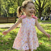 Child in a floral dress running on grass with trees and people in the background
