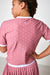 A child wearing a pink short-sleeve top and matching pleated skirt with white polka dots, shown from the back against a plain light background.