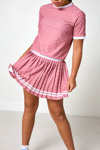 A pink short-sleeve top and pleated mini skirt set with white polka dots and white trim, shown on a model against a plain white studio background.