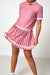 A pink short-sleeve top and pleated mini skirt set with white polka dots and white trim, shown on a model against a plain white studio background.