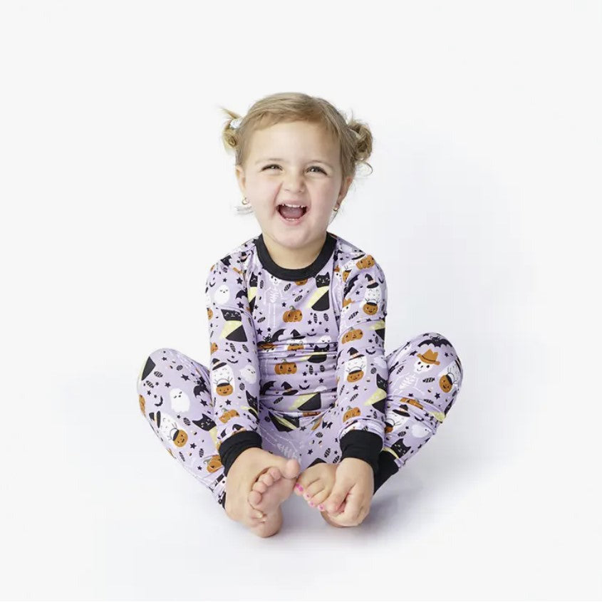 girl wearing long sleeve pajama set in purple spooky cute pattern with ghosts, skeletons, cats and bats