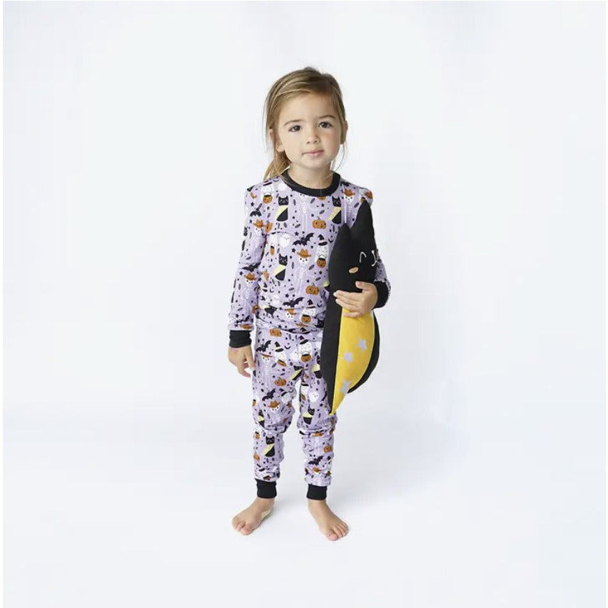 girl wearing long sleeve pajama set in purple spooky cute pattern with ghosts, skeleteons, cats and bats