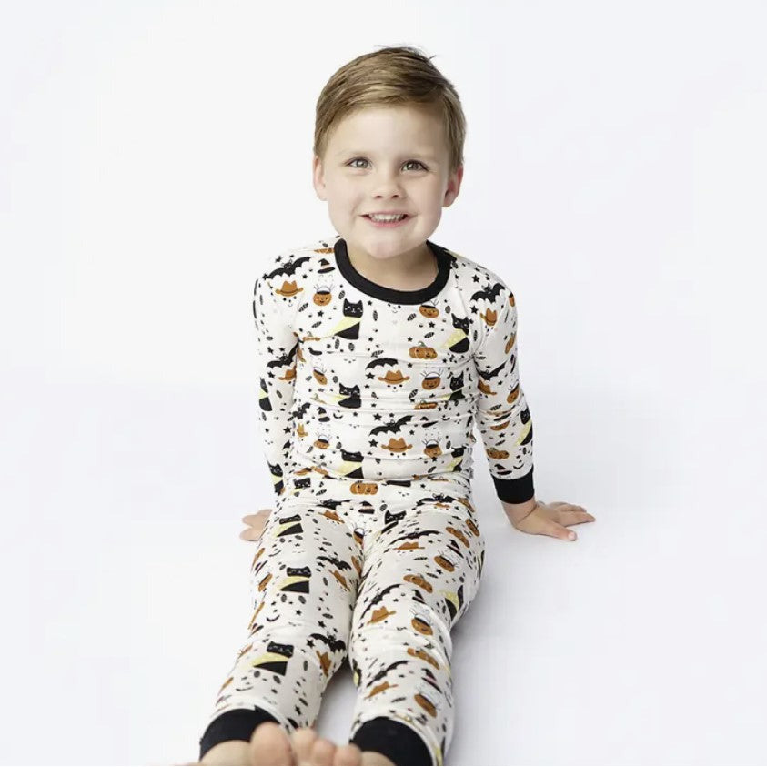boy wearing cream colored long sleeve lounge wear set with spooky cute print with cats, skeletons and ghosts