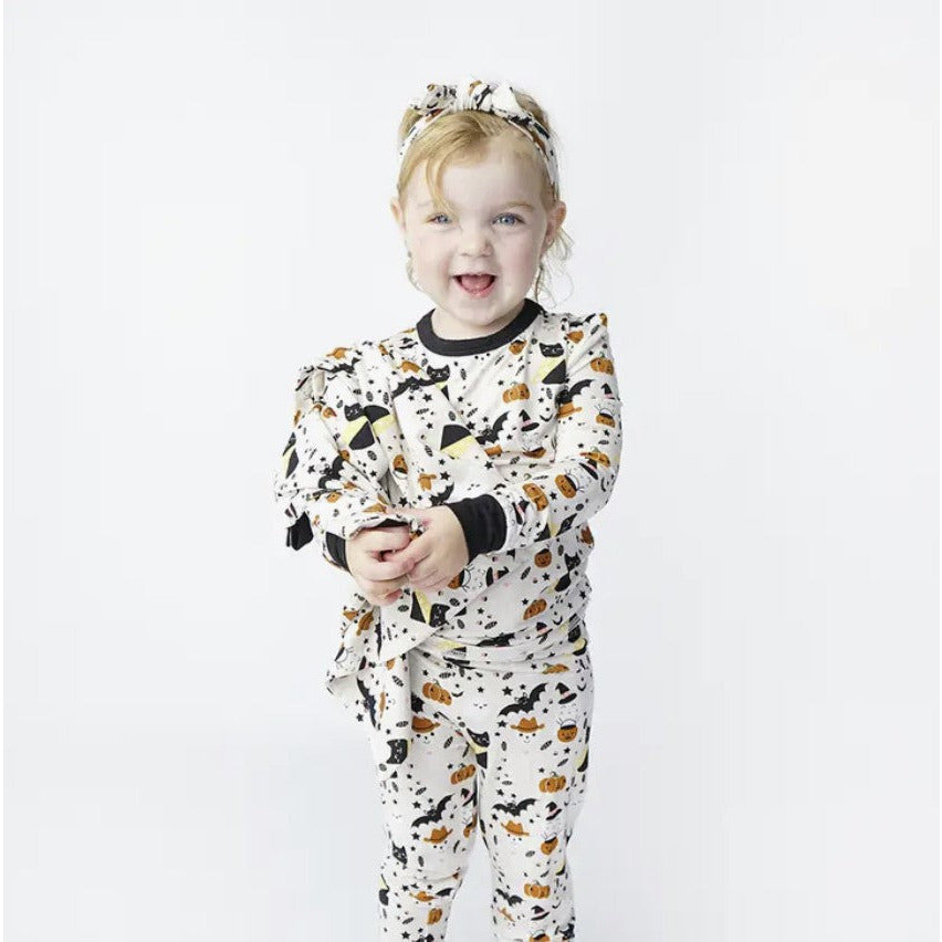 girl wearing cream colored long sleeve lounge wear set with spooky cute print with cats, skeletons and ghosts