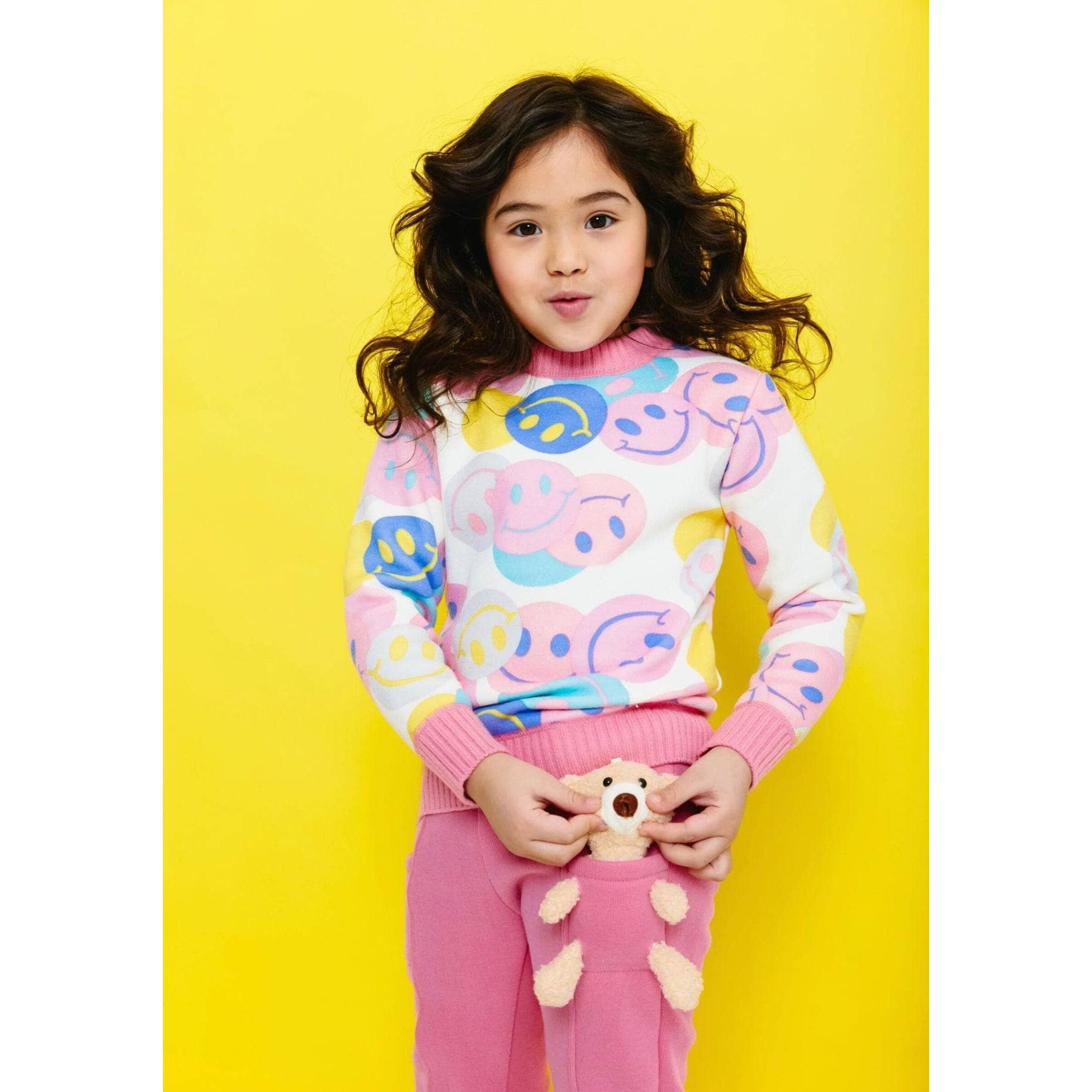 girl wearing white and pink crewneck sweater with multicolored smiley emojis