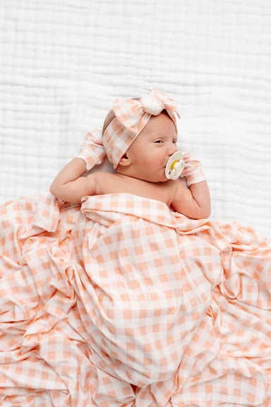 Baby wrapped in a pink and white checkered blanket with a pacifier on a white background