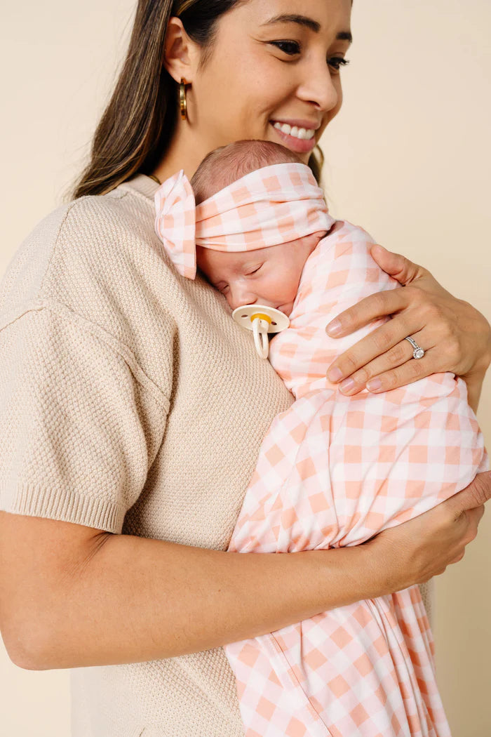 Woman holding a baby wrapped in a pink swaddle against a beige background