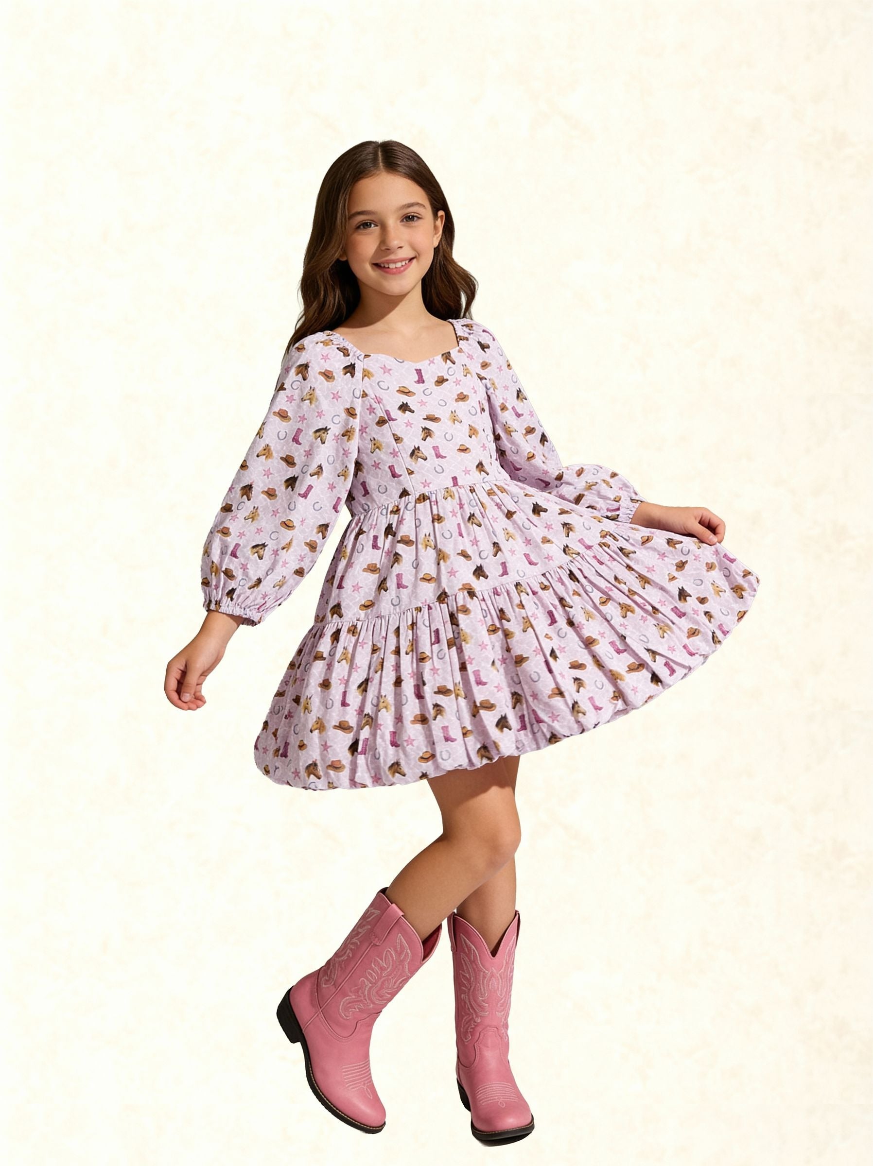 A young girl with long brown hair is wearing a light pink long-sleeve dress with a brown and gold floral pattern, paired with pink cowboy boots, against a textured cream background.