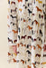 A close-up of a cream-colored dress with a whimsical all-over print of various horse illustrations in brown, black, white, and tan. The dress features tiered ruffles at the waist and cuffs, with a small portion of a model's hand visible on the left side.