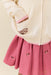 Pink pleated skirt with embroidered horses worn with a cream knit cardigan featuring a front pocket and pink trim by Pink Chicken