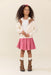 Young girl wearing a pink pleated skirt with horse embroidery styled with a cream cardigan and brown boots from Pink Chicken