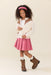 Young girl wearing a pink pleated skirt with horse embroidery a cream cardigan brown boots and a pink headband in a studio setting for Pink Chicken