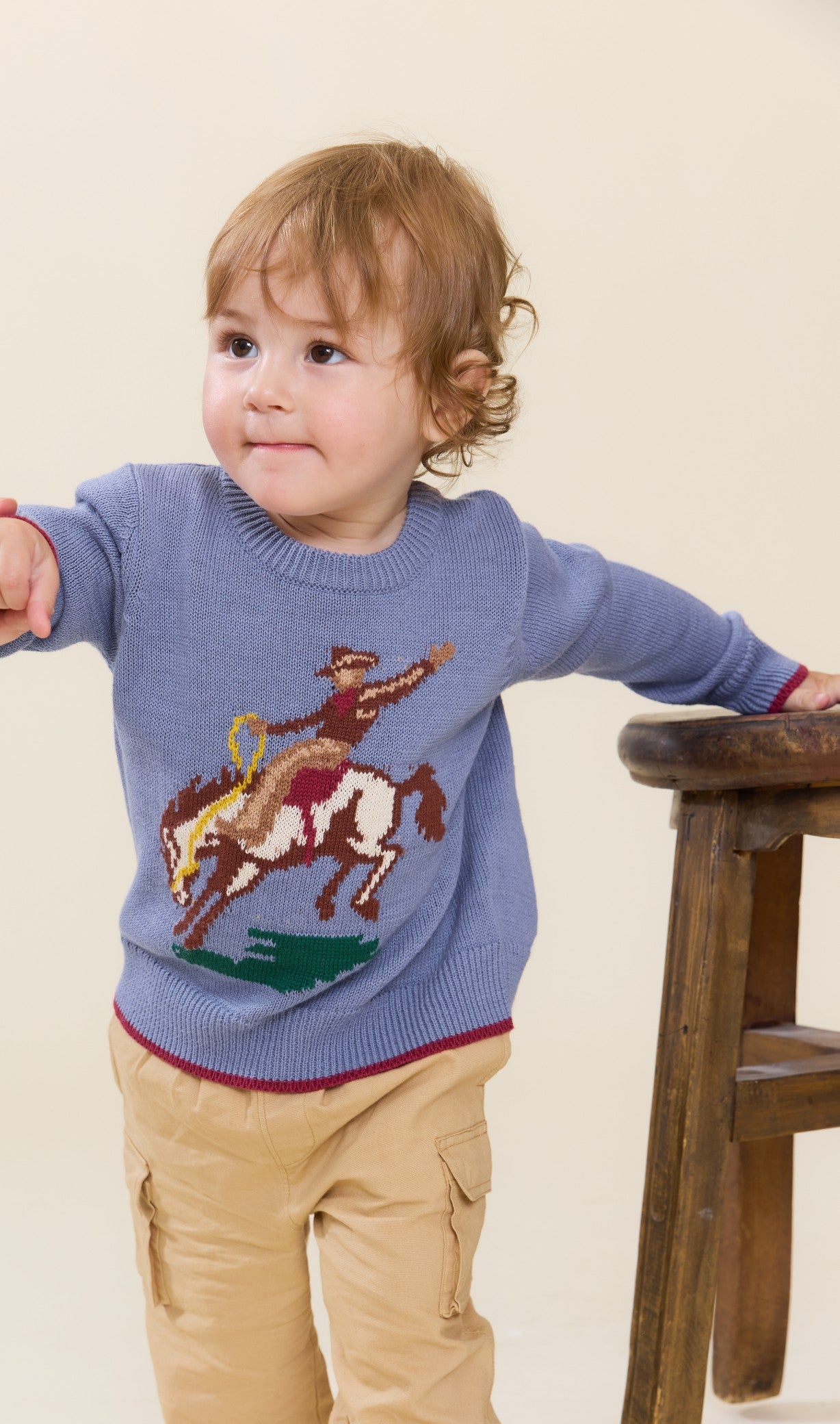 Toddler wearing a blue sweater with a colorful rodeo horse graphic and tan cargo pants by Pink Chicken