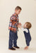 Young boy wearing a brown and multicolor plaid button down shirt holds hands with a toddler in navy overalls from Pink Chicken