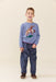 Young boy wearing a blue Pink Chicken sweater with a rodeo horse design and dark patterned pants while standing indoors