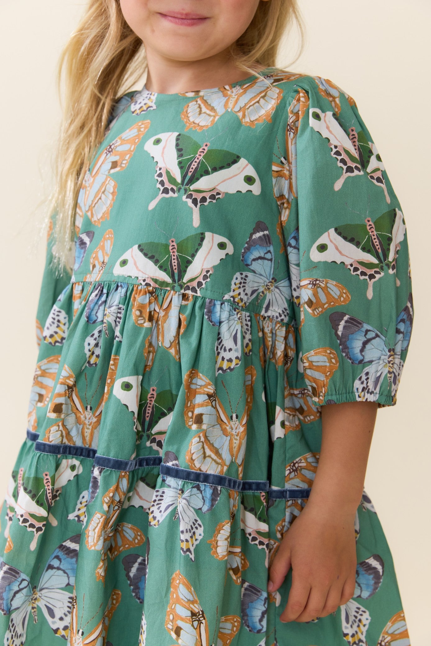 Young girl wearing a Pink Chicken green Maribelle dress with colorful butterfly print gathered tiers and short sleeves