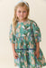 Young girl wearing a green butterfly print dress by Pink Chicken with a gathered waist three quarter sleeves and a flowing skirt