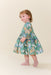 Young girl modeling a green butterfly print dress with long sleeves and a full skirt while wearing pink socks in a studio from Pink Chicken