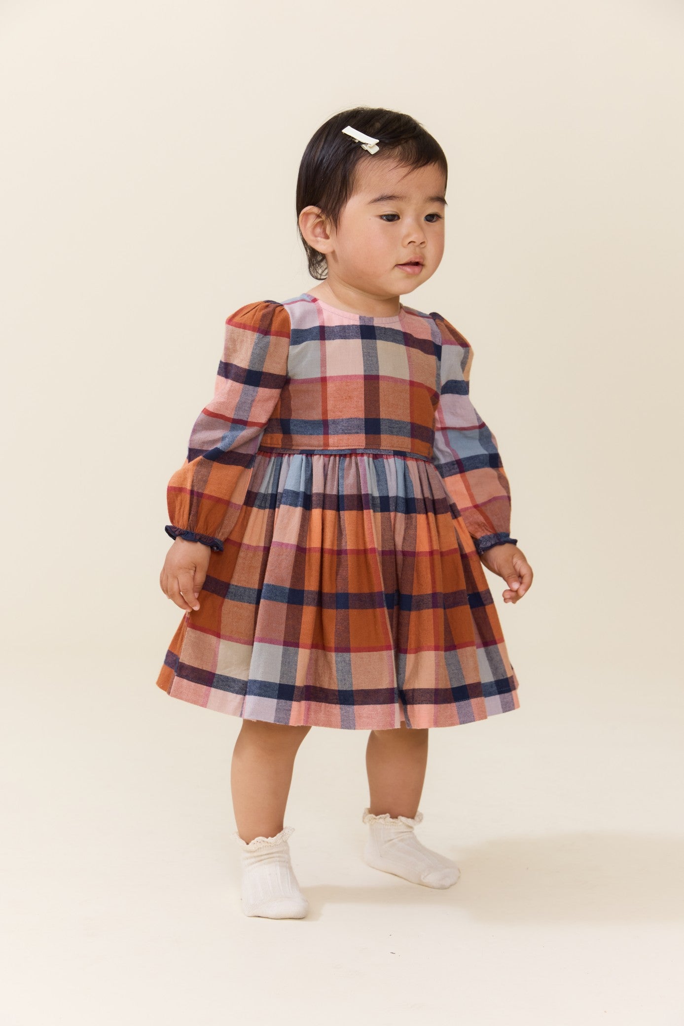 Toddler girl wearing a multicolor plaid long sleeve dress with a gathered skirt and white shoes from Pink Chicken