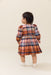 Toddler girl wearing a long sleeve plaid dress with a gathered skirt and white shoes from Pink Chicken posed against a neutral background